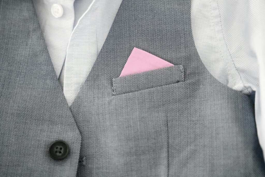 Close-up of a gray vest featuring a pink pocket square, showcasing elegant fashion style.