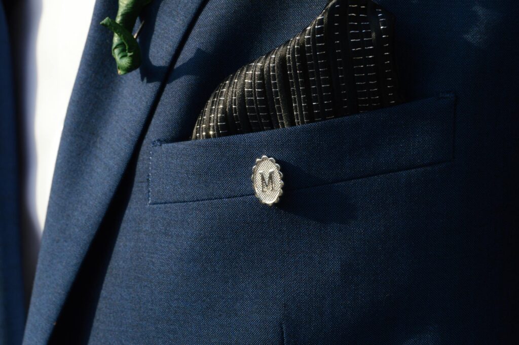 Close-up shot of a navy suit with a monogrammed pin and patterned pocket square.